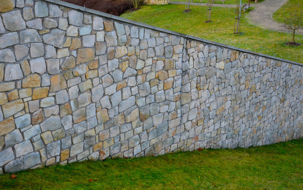 The plank fence follows the sandstone-lined wall that is cracking in several places, the movements of the terrain and the vibrations of the highway car traffic. grassy slope and high wall sloping down - Foto, Imagem