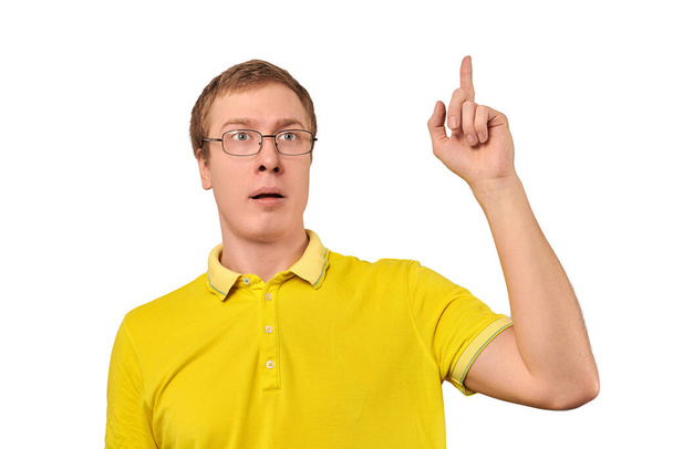 Αστείος νεαρός με διορθωτικά γυαλιά με χειρονομία της εύρηκα, ο άνθρωπος πήρε την ιδέα απομονωμένη σε λευκό φόντο. Έκπληκτος άνθρωπος geek σε κίτρινο T-shirt δείχνοντας δείκτη επάνω, βρήκε λύση για την εργασία - Φωτογραφία, εικόνα