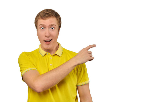 Здивований молодий хлопець зі смішним обличчям у яскраво-жовтій футболці, спрямованій пальцем праворуч, білий ізольований фон. Вражений здивованим обличчям молодого чоловіка в футболці. Портрет збудженого чоловіка
 - Фото, зображення