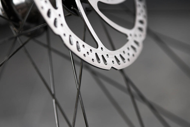 Hydraulic bicycle disk brakes, grey metal disc attached to bike wheel close up, effective popular mountain bicycle brakes. Hydraulic disk brakes on bicycle wheel, bicycle spokes gray background - Foto, imagen