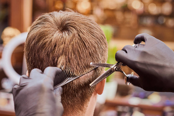 Мужская стрижка в парикмахерской крупным планом, клиент стрижется у парикмахера гребнем и ножницами. Парикмахер делает прическу в парикмахерской, новая стильная современная прическа для мужчин - Фото, изображение