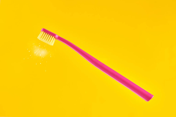 Pink toothbrush on yellow background for oral hygiene to clean teeth, gums and tongue. Manual plastic toothbrush with fresh shine near bristle isolated on yellow background - Photo, image