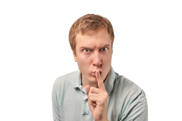 Funny guy in light gray Polo T-shirt asking to be quiet, silence gesture isolated on white background. Young man saying Shhh, keep quiet, please and making silence gesture, request for silence - Photo, image