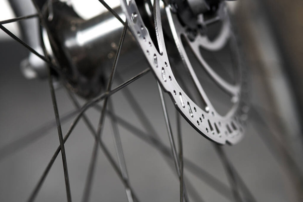 Bicycle disk brakes close up, grey metal disc attached to bike wheel, effective popular mountain bicycle brakes. Hydraulic disk brakes on bicycle wheel, bicycle spokes gray background - Foto, Imagem
