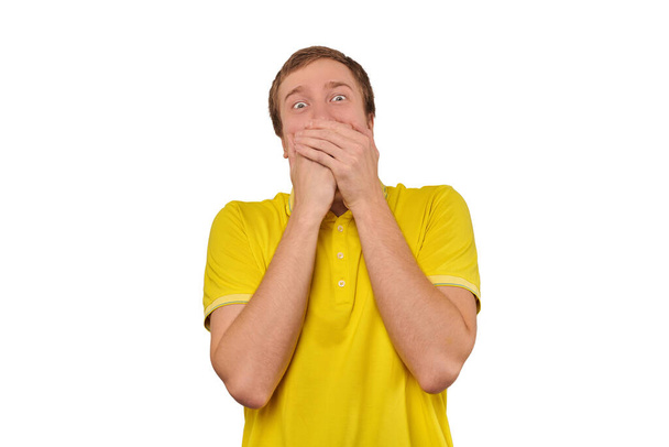 Funny guy loudly laughing out loud covering mouth with hands isolated on white background. Young man in casual yellow T-shirt laughing loudly trying to keep emotions from surprise, happy expression - Foto, Imagen