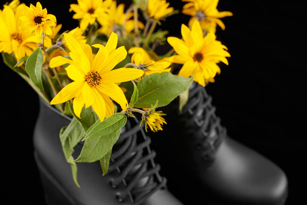 Черные женщины платформы сапоги с букетом желтого Иерусалима артишоки цветы крупным планом, черный фон. Цветы подсолнуха в ботинках на высоком каблуке, женственность в обуви - Фото, изображение