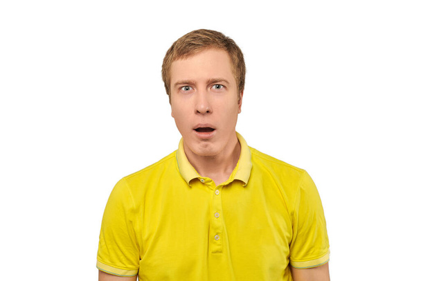 Puzzled young guy with funny face and open mouth in yellow Polo T-shirt, white isolated background. Confused young man close up on white background. Portrait of amazed man in yellow Polo T-shirt - Foto, Imagem