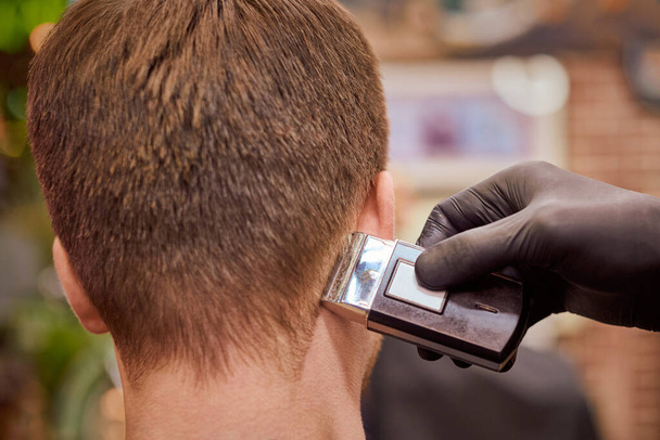 Мужская стрижка бритья в парикмахерской, клиент получает стрижку парикмахером с электробритвой. Парикмахер делает прическу в парикмахерской, новая стильная современная прическа для мужчин - Фото, изображение