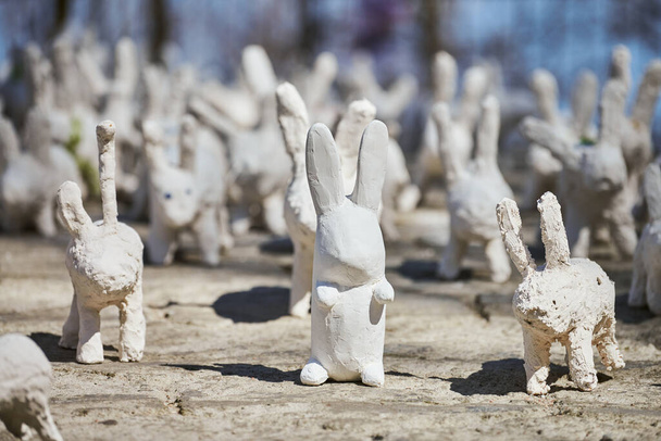 White rabbit statues made of plaster at outdoor art exhibition, artificial white hares on city street. A lot of white handmade rabbits, many decorative bunnies, Easter urban decor concept - Photo, image