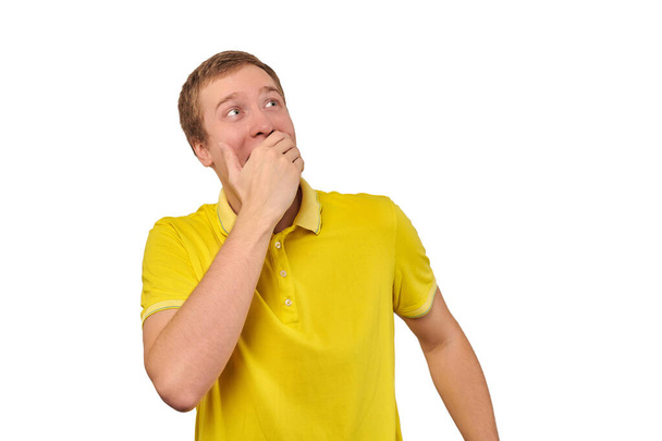 Funny guy loudly laughing out loud covering mouth with hands isolated on white background. Young man in casual yellow T-shirt laughing loudly trying to keep emotions from surprise, happy expression - Zdjęcie, obraz