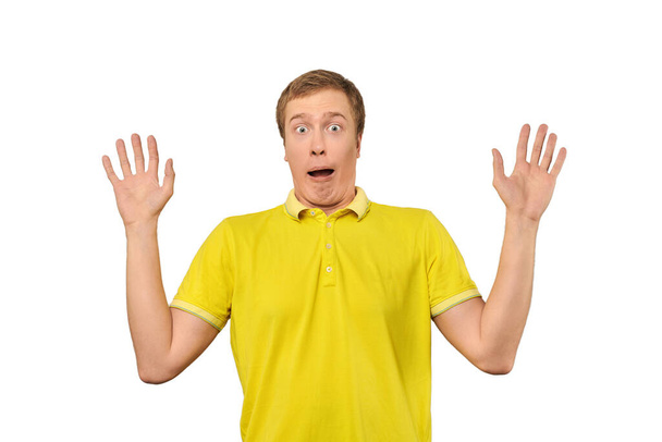 Scared young man in yellow T-shirt with hands up, white isolated background. Afraid facial expression of young man in yellow Polo isolated on white background. Portrait of frightened man - Photo, image