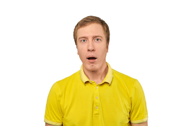 Puzzled young guy with funny face and open mouth in yellow Polo T-shirt, white isolated background. Confused young man close up on white background. Portrait of amazed man in yellow Polo T-shirt - Foto, Imagen