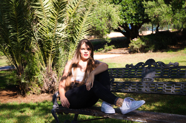 Bella giovane donna con i capelli biondi e gli occhi azzurri siede sulla panchina del parco e posa per la foto come un modello. Lei è felice di fare diverse posture del corpo ed espressioni. - Foto, immagini