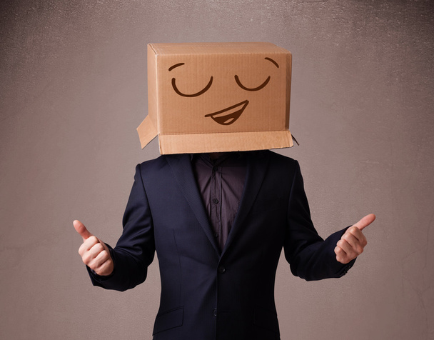 Young man gesturing with a cardboard box on his head with smiley - Foto, Imagen