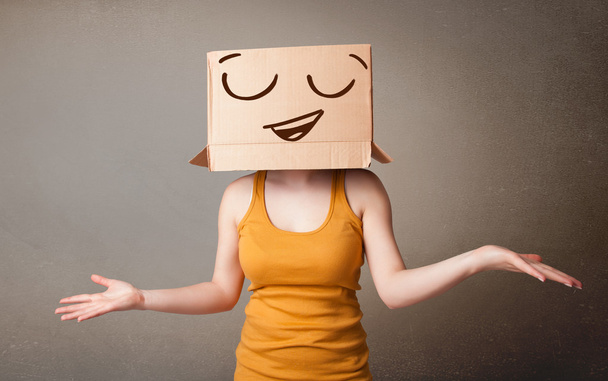 Young woman gesturing with a cardboard box on her head with smil - 写真・画像
