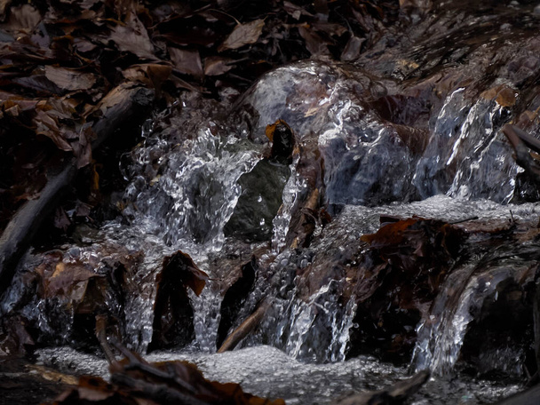 A beautiful small flowing river due to snow melt forming a clean cascade with fresh cool water surrounded by vegetation on a wild stone mountain - Foto, Bild