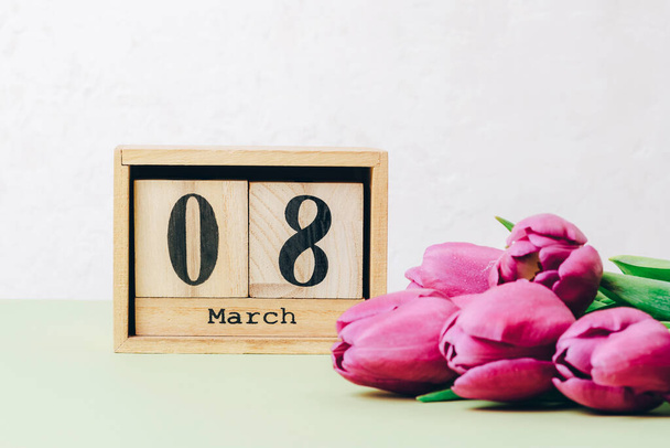 Bunch of purple tulips and wooden block calendar with 8 march date on a table. Womens day holiday concept, closeup. - Photo, image