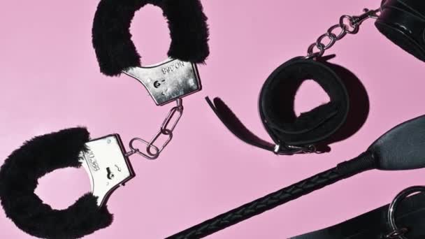 Handcuffs, whip flogger for BDSM sex with submission and domination. A set of adult intimate erotic sex toys on a pink background - Záběry, video