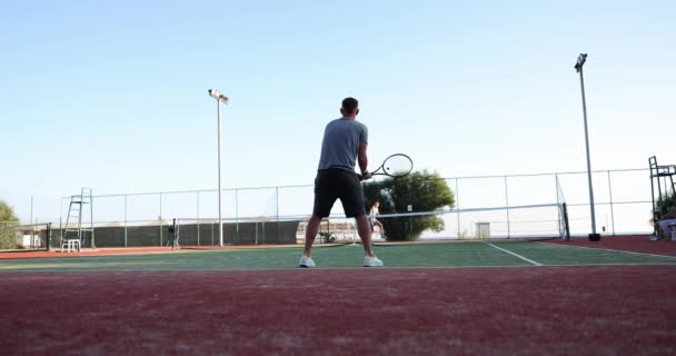 Tennispelaajat pelaavat tennistä aurinkoisena päivänä kentällä. Mies tennispelaaja lyödä pallo - Materiaali, video