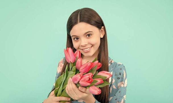 nastolatka dziewczyna z wiosennym bukietem na niebieskim tle. kwiatowy prezent. Szczęśliwe dziecko lubi tulipany. Dzień matki lub kobiety. dziecko trzymać kwiaty na 8 marca. - Zdjęcie, obraz