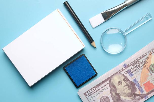 A flatlay picture of fingerprint pad on fake cash, copyspace notepad, pencil magnifying glass, safety glass, puffer, brush and inkpad. Forensic accounting concept. - Foto, Bild