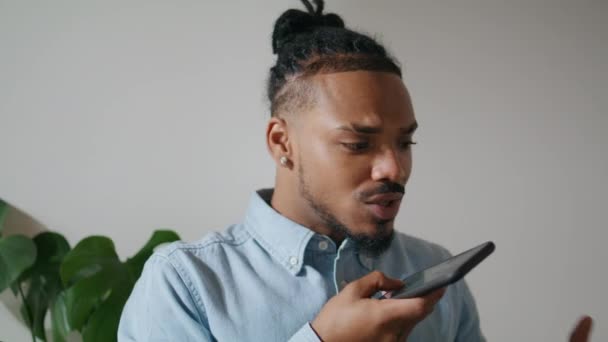 Σύγχρονος άντρας μιλάει στο τηλέφωνο στο κοντινό γραφείο. Θετικός Αφροαμερικάνος ελεύθερος επαγγελματίας ηχογραφεί φωνητικό μήνυμα smartphone. Μαύρος κομμωτής που μιλάει για κινητό μεγάφωνο που δουλεύει σε απομακρυσμένο στούντιο  - Πλάνα, βίντεο