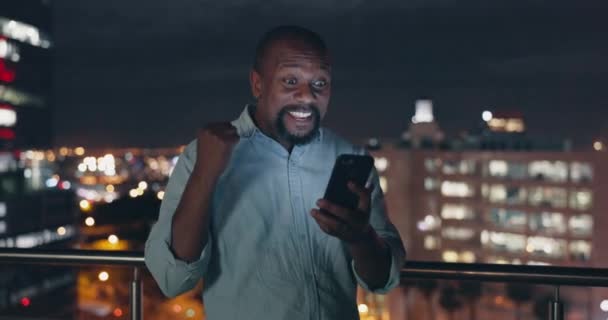 Success, celebration and black man with phone on city rooftop at night. Winner, wow and surprised businessman fist pump with 5g mobile smartphone in town celebrating win, good news or financial goals. - Imágenes, Vídeo