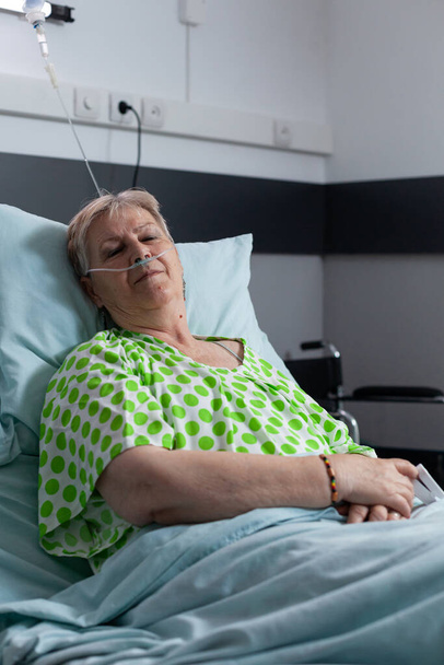 Stará dáma odpočívá v posteli v nemocničním pokoji. Starší žena sedativa na operaci na klinice. Starší ženy odpočívají, spí, zotavují se z infekce. Pacient s onemocněním pomocí lékařské pomoci pro dýchání. - Fotografie, Obrázek