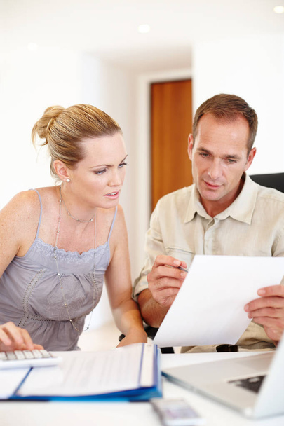 Going over the monthly bills...a woman and a man looking at paperwork with a laptop in front of them - Photo, Image