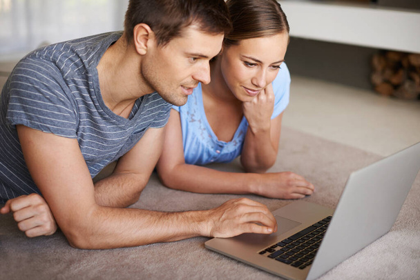 Browsing their options online. a young couple using a laptop together on the floor of their home - Foto, imagen