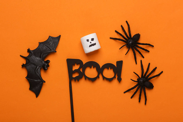 Aranhas de plástico com morcego, marshmallow e palavra boo! sobre fundo laranja. Decoração de Halloween. Vista superior - Foto, Imagem