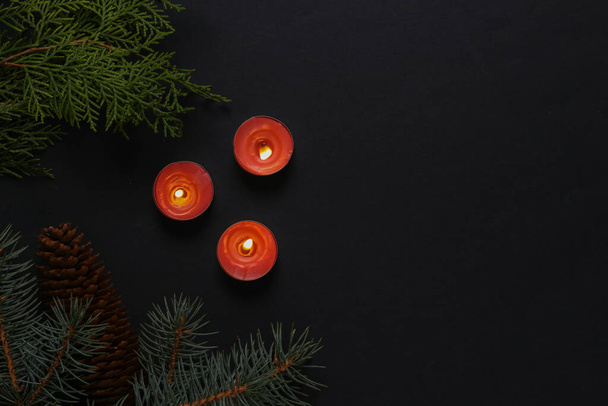 Rode vlammende aroma kaarsen met een kerstboom tak. Kerstmysterie. Aromatherapie, schoonheid, spa. Zwarte achtergrond. - Foto, afbeelding
