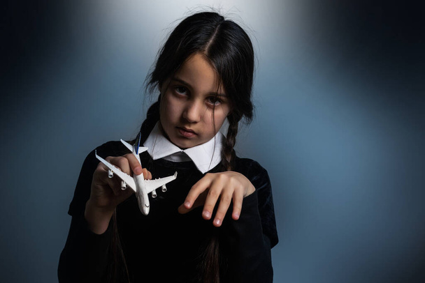 おもちゃの飛行機と暗い背景にゴシック様式の組紐の女の子. - 写真・画像