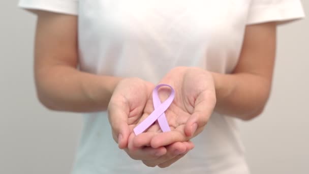 Día Mundial del Cáncer, 4 de febrero. Mano de mujer sosteniendo la cinta púrpura lavanda para apoyar a las personas que viven y enferman. Salud y concepto médico - Imágenes, Vídeo