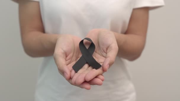 Mujer sosteniendo cinta negra para el melanoma y el cáncer de piel, mes de conciencia de lesiones de vacunas, dolor y descanso en paz. Concepto sanitario y racista - Imágenes, Vídeo