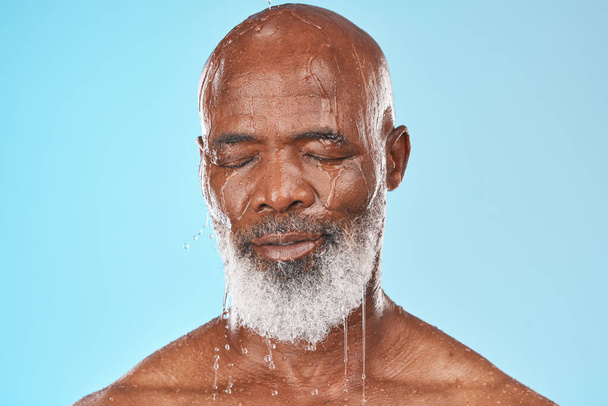 Black man, face and water drip on studio blue background for wellness, healthy skincare and bathroom hygiene. Male model, wet shower and water drops for mature beauty, facial and fresh body cleaning. - Fotografie, Obrázek