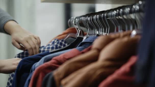 Mulher olha através das jaquetas e camisas no shopping
 - Filmagem, Vídeo