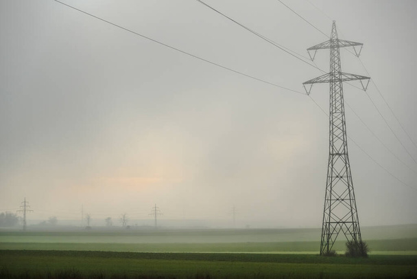 один столб мощности с плотным туманом над полями в зимний период - Фото, изображение