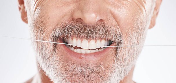 Dental, floss and mouth of senior man in studio isolated on a gray background. Hygiene, cleaning and elderly male model with product flossing teeth for oral wellness, tooth care and healthy gums - Photo, Image