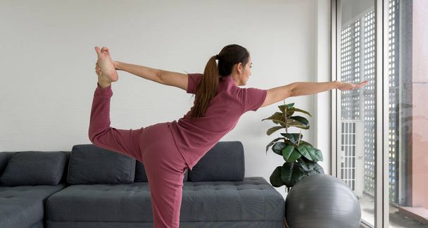 Ev ödevi sırasında Natarajasana Poose egzersizi yapan Asyalı ev hanımı. Kadın, oturma odasında Lord of the Dance Poose 'da yoga yapıyor.. - Fotoğraf, Görsel