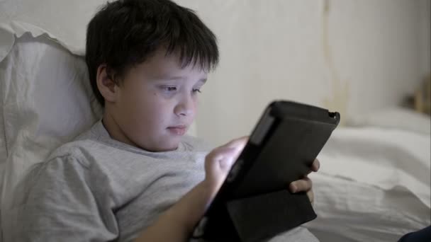 Teenager boy using tablet computer lying in bed - Filmati, video