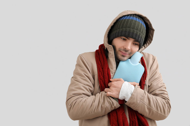 Young man in winter clothes with hot water bottle on grey background - Fotografie, Obrázek