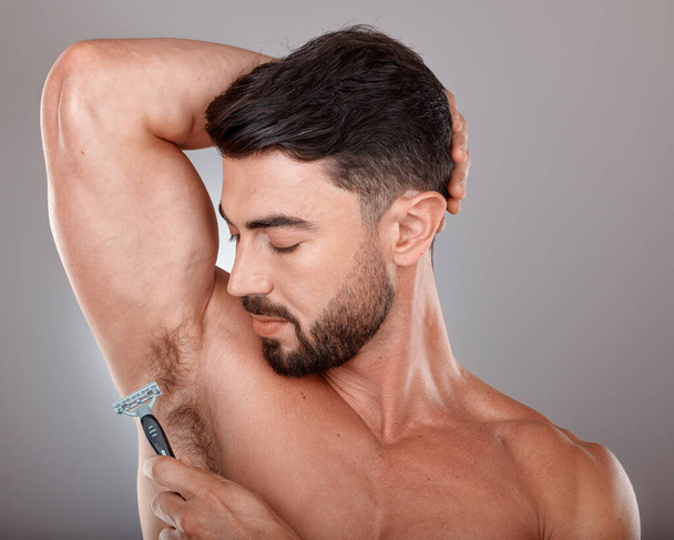 Cosmetics, shaving armpit and man with skincare, hygiene and wellness on grey studio background. Male, guy and razor for hair removal, grooming and treatment for morning routine, fresh and beauty. - Foto, afbeelding