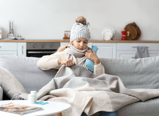 Ill girl with hot water bottle sitting on sofa at home - Fotografie, Obrázek