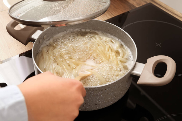 Woman preparing delicious pasta on electric stove in kitchen - Zdjęcie, obraz