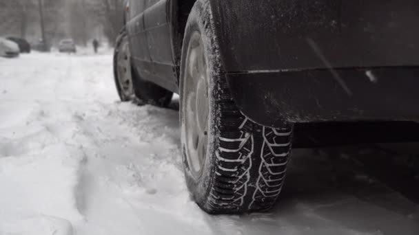 Car is parked in parking lot. Snow storm and lots of snow on car. It's snowing. Winter tires close-up. Poor road conditions. Slippery and cold. Snowstorm. abandoned autobile. - Video, Çekim