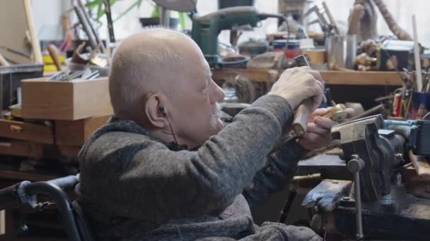 Senior elderly master jeweler in wheelchair works in a workshop with a vice - Metraje, vídeo