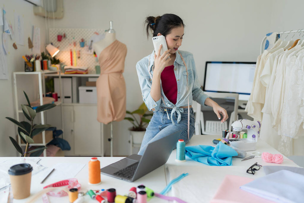 Kobieta-przedsiębiorca pracująca na czacie mobilnym w studiu krawieckim Jest projektantką tekstyliów produkującą nowe kolekcje przy użyciu najnowocześniejszych technologii. - Zdjęcie, obraz
