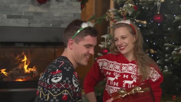 CLOSE UP: Young man gives his lady a Christmas gift and receives a grateful hug. Cheerful couple celebrates winter holidays in a beautifully decorated home and exchanges presents on festive evening. - Filmati, video