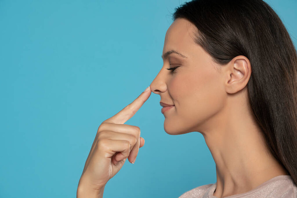 Profil mladé ženy dotýkající se jejího nosu na modrém pozadí studia - Fotografie, Obrázek